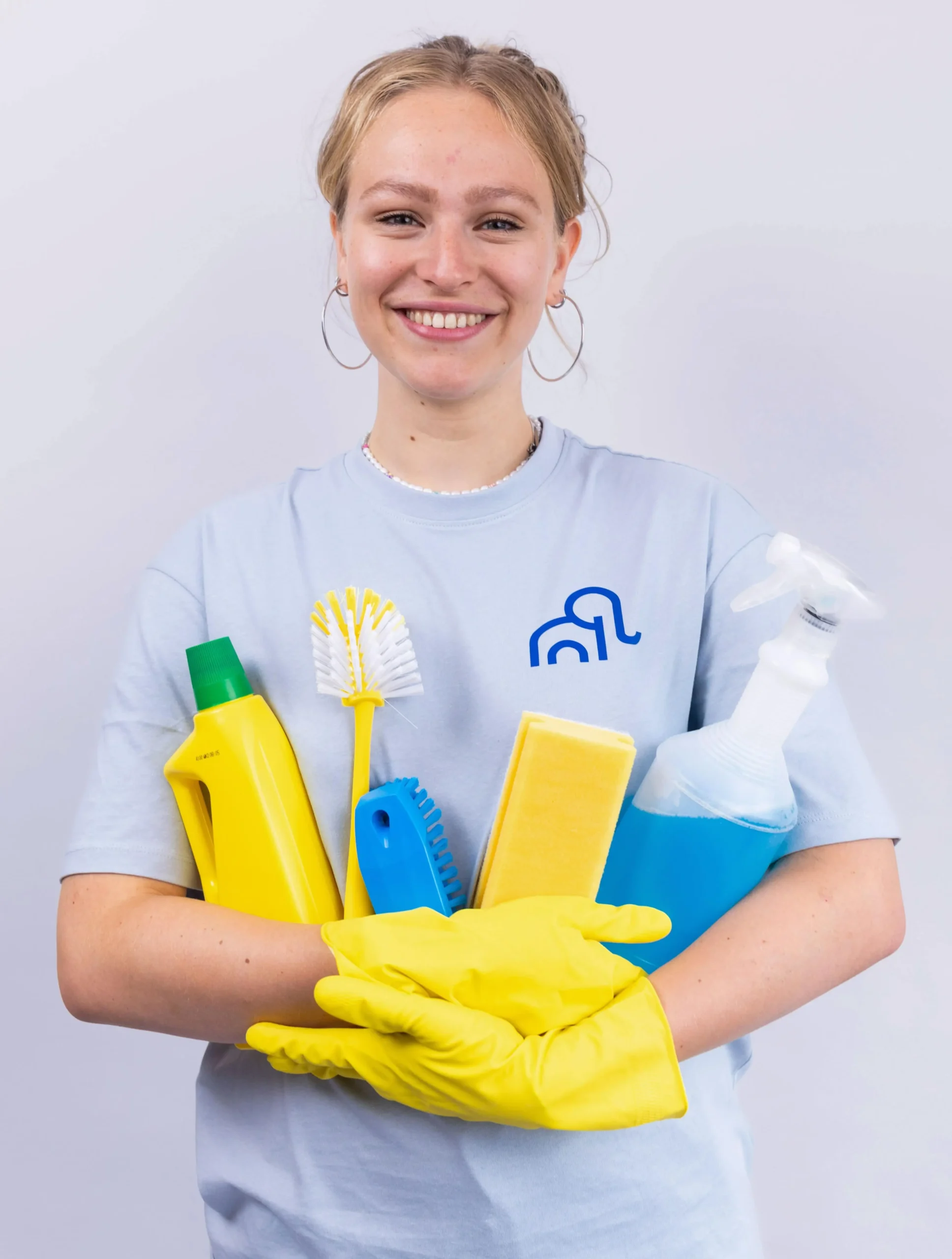 een vrouwelijke medewerker met verschillende schoonmaakmiddelen in haar armen