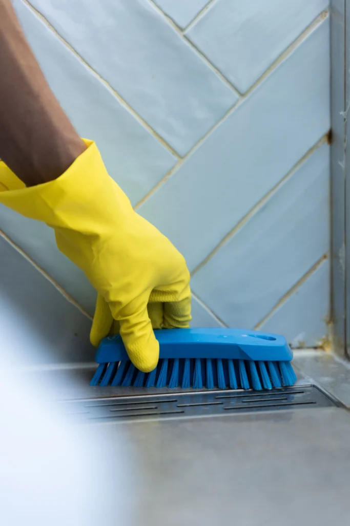 een gele handschoen met blauwe borstel die schimmel verwijderd in een badkamer