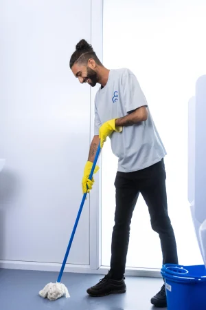 een medewerker van clean and clever die de sanitair dweilt met een blauwe dweil en gele handschonen